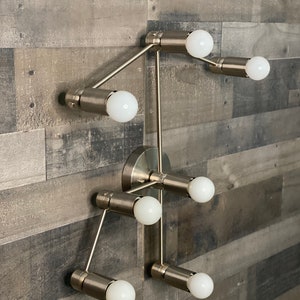 May include: A silver metal light fixture with six light bulbs. The fixture is mounted on a wall and has a modern design.