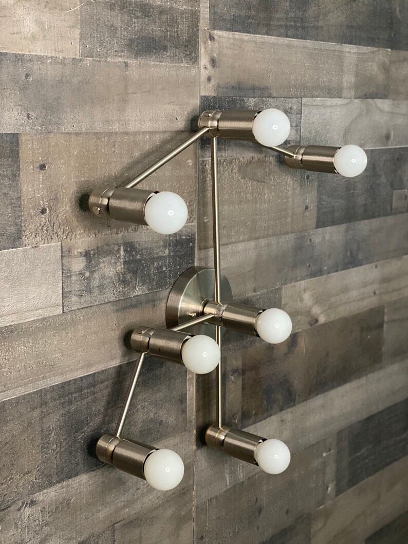 May include: A silver metal light fixture with six light bulbs. The fixture is mounted on a wall and has a modern design.
