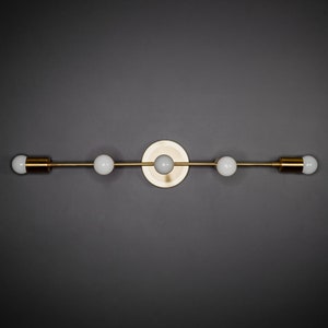 May include: A gold-toned wall sconce with four light bulbs. The sconce has a circular base and a long, straight arm with the bulbs evenly spaced along it.