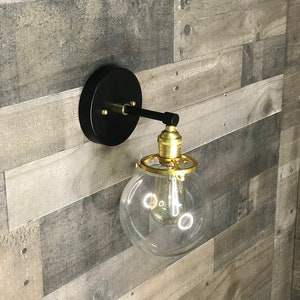 May include: A black wall sconce with a gold finish and a clear glass globe light fixture.