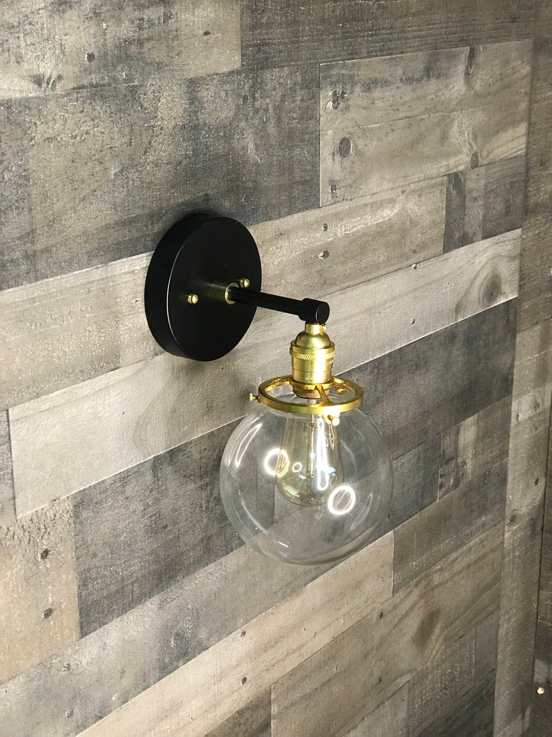 May include: A black wall sconce with a gold finish and a clear glass globe light fixture.