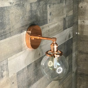May include: A copper wall sconce with a clear glass globe shade. The sconce has a simple design and is perfect for adding a touch of modern style to any room.