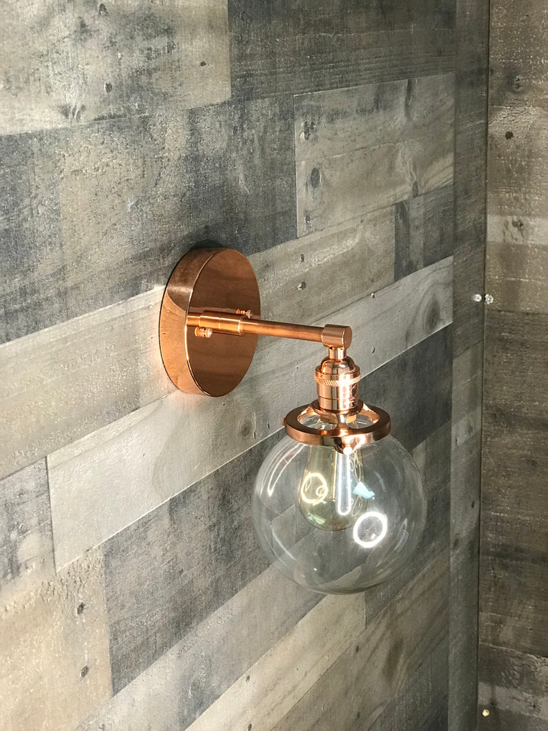 May include: A copper wall sconce with a clear glass globe shade. The sconce has a simple design and is perfect for adding a touch of modern style to any room.
