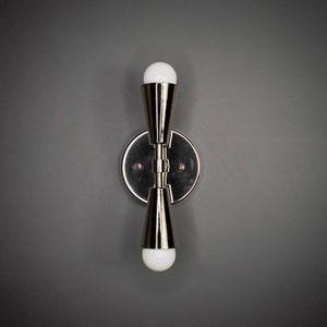 以下が含まれることがあります： 2つの電球が付いた銀色の壁掛け照明。照明は丸いベースと2つの円錐形のシェードを持っています。