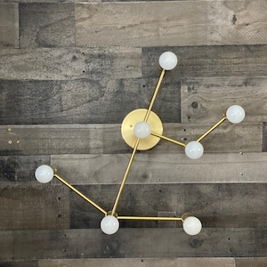 May include: A gold metal light fixture with six white globe light bulbs. The fixture is mounted on a wood wall.