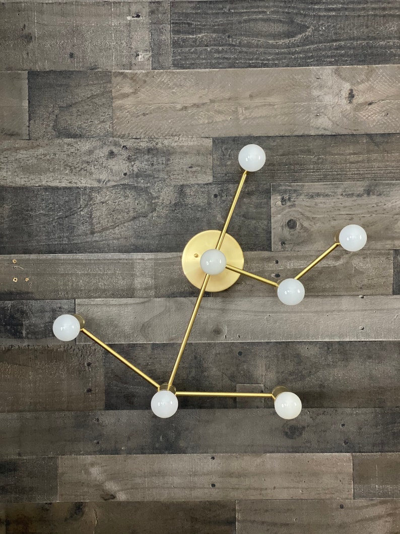 May include: A gold metal light fixture with six white globe light bulbs. The fixture is mounted on a wood wall.