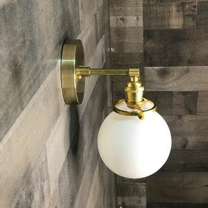 May include: A gold wall sconce with a white frosted glass globe shade. The sconce has a simple design with a single bulb.
