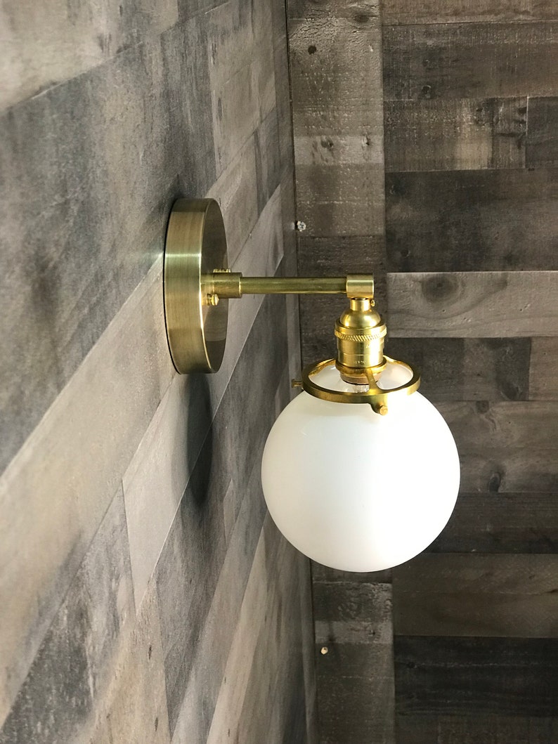 May include: A gold wall sconce with a white frosted glass globe shade. The sconce has a simple design with a single bulb.