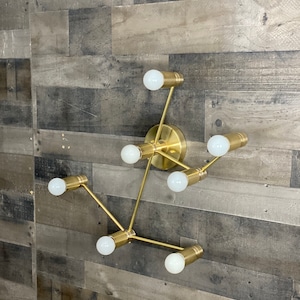 May include: A gold-toned metal wall sconce with six light bulbs. The sconce has a modern, geometric design with a branching structure.
