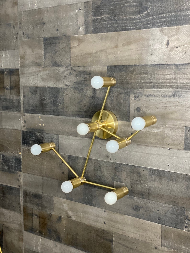 May include: A gold-toned metal wall sconce with six light bulbs. The sconce has a modern, geometric design with a branching structure.