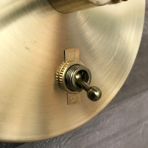 Puede incluir: Un interruptor de luz de pared dorado con una perilla redonda y las palabras "ON" y "OFF" impresas en el interruptor.