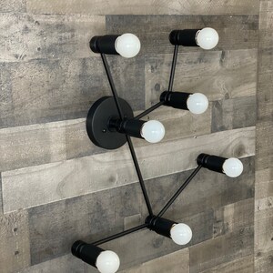 May include: A black metal wall sconce with six light bulbs. The sconce has a modern design with a circular base and multiple arms extending out.