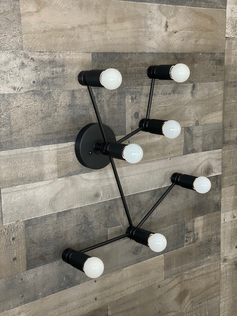 May include: A black metal wall sconce with six light bulbs. The sconce has a modern design with a circular base and multiple arms extending out.