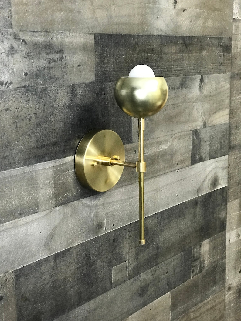May include: A gold wall sconce with a round, globe-shaped light fixture. The sconce has a simple, modern design and is perfect for adding a touch of elegance to any room.