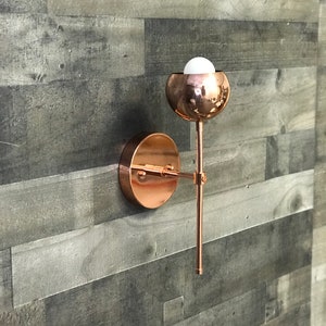 May include: A copper wall sconce with a round, globe-shaped light fixture. The sconce has a simple, modern design and is perfect for adding a touch of elegance to any room.