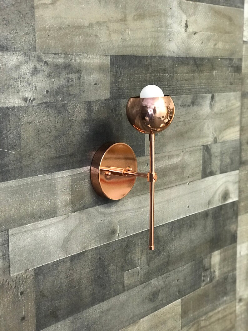 May include: A copper wall sconce with a round, globe-shaped light fixture. The sconce has a simple, modern design and is perfect for adding a touch of elegance to any room.