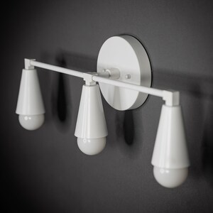 May include: White wall-mounted light fixture with three cone-shaped shades and exposed bulbs.