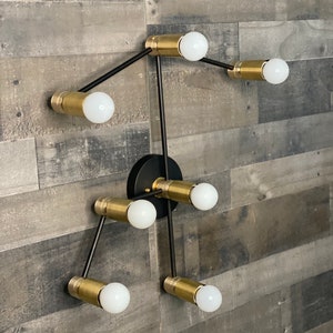 May include: A modern black and gold wall sconce with six light bulbs. The sconce has a geometric design with arms extending out from a central point.