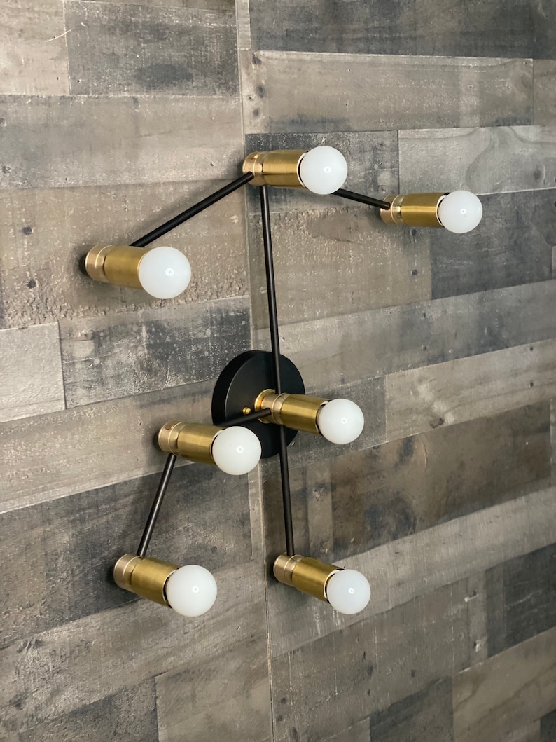 May include: A modern black and gold wall sconce with six light bulbs. The sconce has a geometric design with arms extending out from a central point.