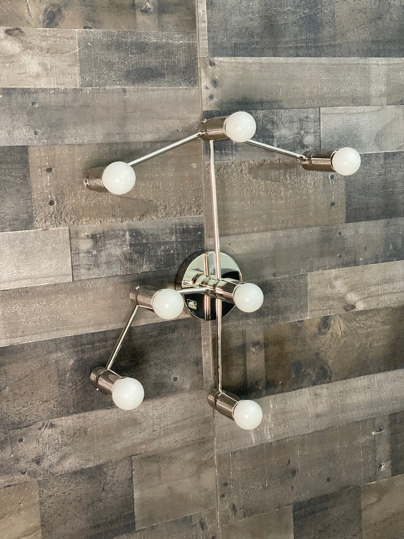 May include: A modern, silver-toned wall sconce with six light bulbs. The sconce has a geometric design with multiple arms extending from a central hub.