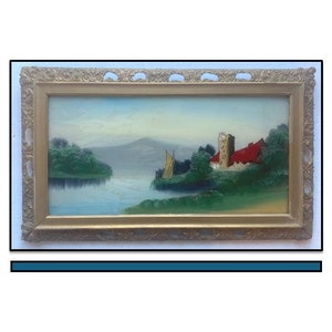 May include: A framed oil painting depicting a lake scene with a red building on the shore, a sailboat on the water, and a mountain in the background.