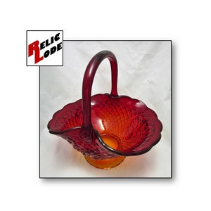 Puede incluir: Una cesta de vidrio roja con un borde festoneado y un asa. La cesta está hecha de vidrio transparente con un tinte rojo y tiene un patrón texturizado.