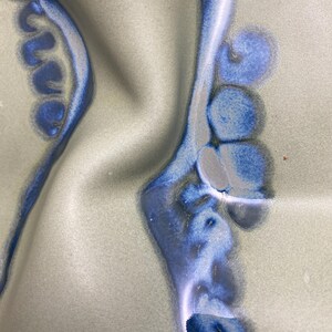 May include: Close-up of a ceramic surface with a blue and white glaze. The glaze has a swirling pattern, creating a unique and abstract design.