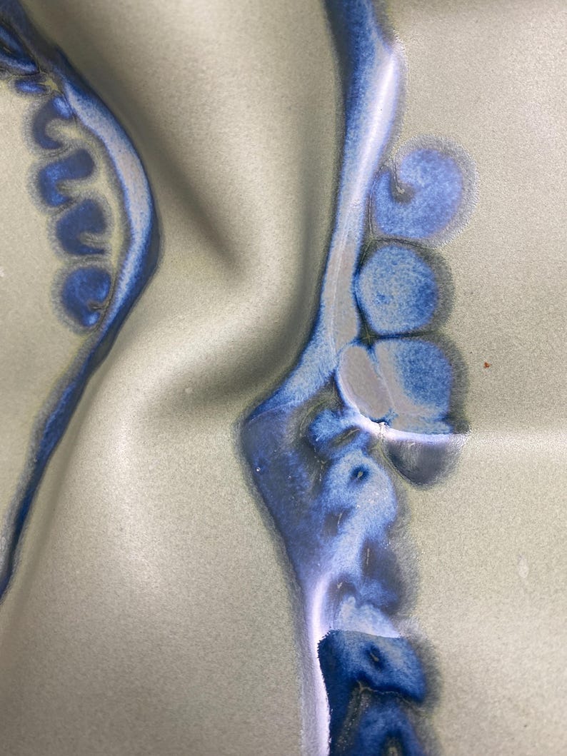 May include: Close-up of a ceramic surface with a blue and white glaze. The glaze has a swirling pattern, creating a unique and abstract design.