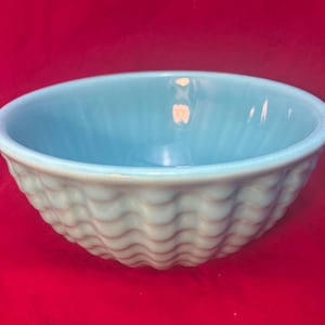 May include: A light blue ceramic bowl with a wavy, textured exterior. The bowl has a smooth, rounded rim and a solid light blue interior. The bowl is likely used for serving food or as a decorative piece.