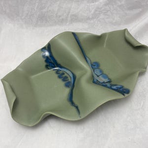 May include: A green ceramic serving dish with blue and white glaze. The dish has a wavy, organic shape.