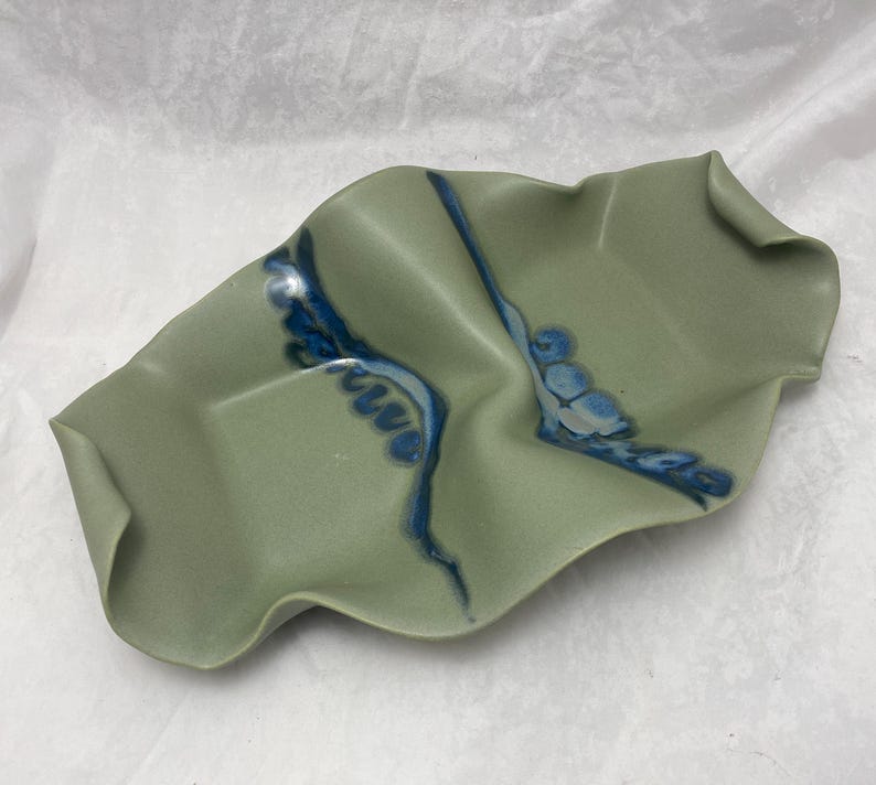 May include: A green ceramic serving dish with blue and white glaze. The dish has a wavy, organic shape.