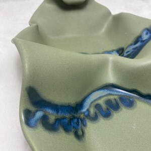 May include: A green ceramic serving dish with a blue and white glaze. The dish has a wavy, organic shape.