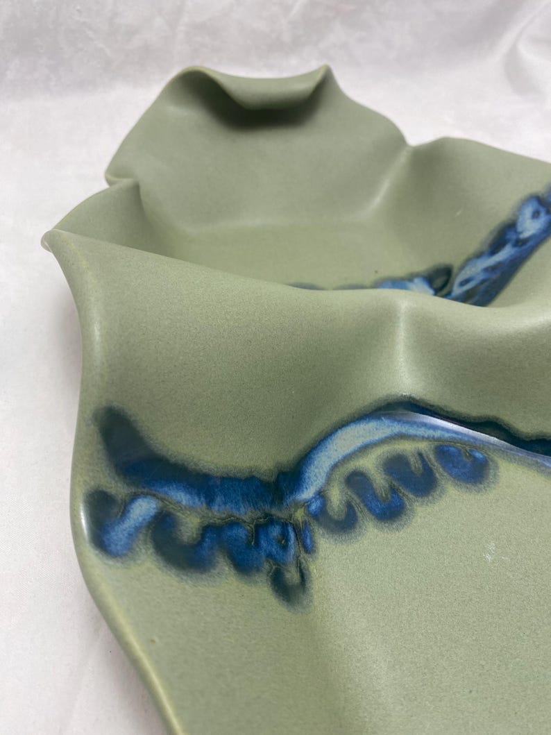 May include: A green ceramic serving dish with a blue and white glaze. The dish has a wavy, organic shape.
