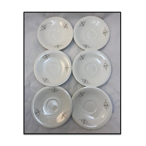 May include: Set of six white ceramic saucers with a silver abstract design. The saucers are perfect for serving coffee or tea.