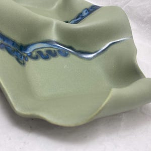 May include: A green ceramic dish with a wavy edge and blue and white glaze. The dish has a unique, organic shape.