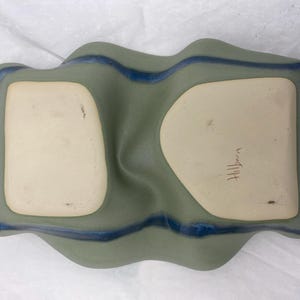 May include: A green ceramic serving dish with two indented sections. The dish has a blue glaze around the edges and the word "Hilltop" is written in brown ink on the bottom.