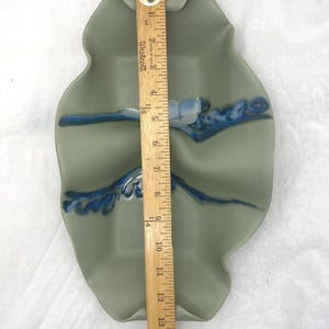 May include: A light green ceramic serving dish with three sections. The dish has a wavy, organic shape and is decorated with blue and white glaze. The dish is approximately 15 inches long.