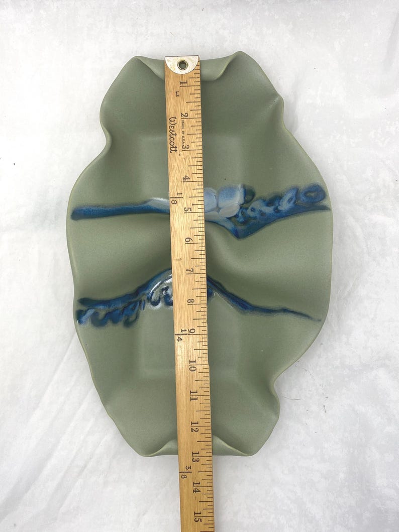 May include: A light green ceramic serving dish with three sections. The dish has a wavy, organic shape and is decorated with blue and white glaze. The dish is approximately 15 inches long.