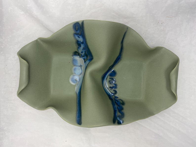 May include: A green ceramic serving dish with two divided sections. The dish has a wavy edge and is decorated with blue and white floral designs.