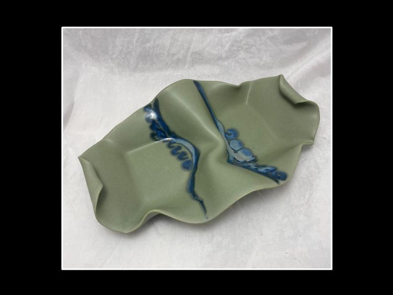 May include: A green ceramic serving dish with a wavy, organic shape. The dish has a blue and white glaze design.