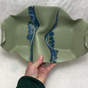 May include: A green ceramic serving dish with blue and white abstract designs. The dish has a wavy, organic shape.