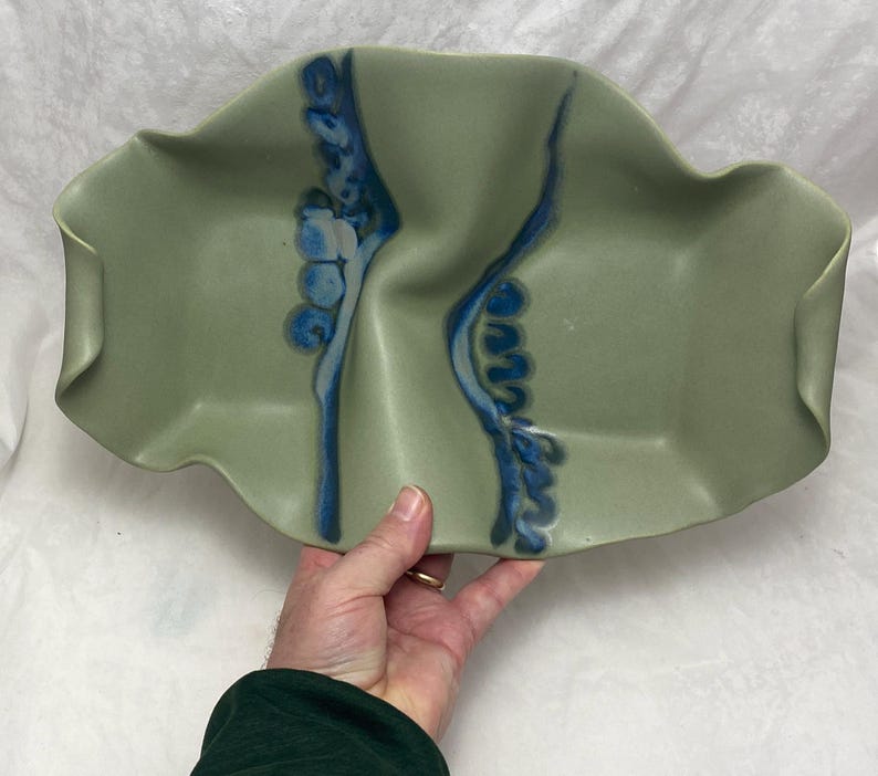 May include: A green ceramic serving dish with blue and white abstract designs. The dish has a wavy, organic shape.