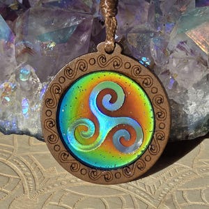 以下が含まれることがあります： 虹色のトリケトラシンボルが描かれた円形のデザインのウッドペンダント。ペンダントは茶色の紐につけられています
