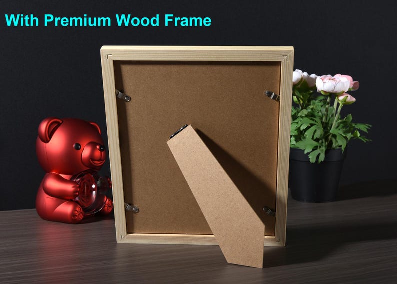 May include: A wooden picture frame with a light brown finish. The frame is standing on a brown surface with a red teddy bear in the foreground. The frame has a cardboard backing and a kickstand.