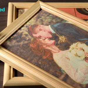 May include: A framed photo of a couple kissing, engraved on a wooden surface. The photo is in a light wood frame with a raised edge.