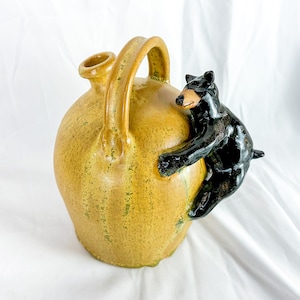 May include: A yellow ceramic jug with a black bear figurine climbing up the side.