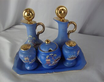 May include: A blue ceramic condiment set with gold accents. The set includes two bottles, two shakers, and a lidded sugar bowl, all on a matching tray. Each piece features a gold lid and handle, with painted Asian-inspired landscape designs.