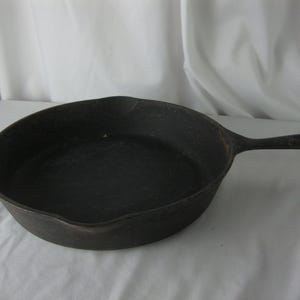 May include: A well-seasoned, cast iron skillet with a long handle and a rounded cooking surface. The skillet is dark gray and shows signs of use, indicating it's ready for cooking. The handle has a hole for hanging.