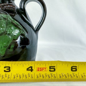 Puede incluir: Una jarra de cer&aacute;mica negra y verde con asa. La jarra tiene un dise&ntilde;o de hoja verde y mide aproximadamente 12,7 cm de alto.