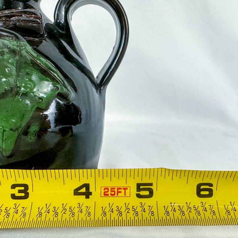 Puede incluir: Una jarra de cer&aacute;mica negra y verde con asa. La jarra tiene un dise&ntilde;o de hoja verde y mide aproximadamente 12,7 cm de alto.
